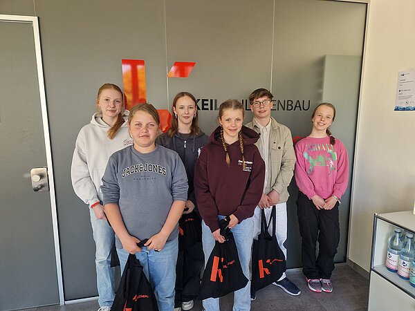 [Translate to Spanish:] Schüler stehen mit Geschenktüten vor dem Logo von Keil Anlagenbau